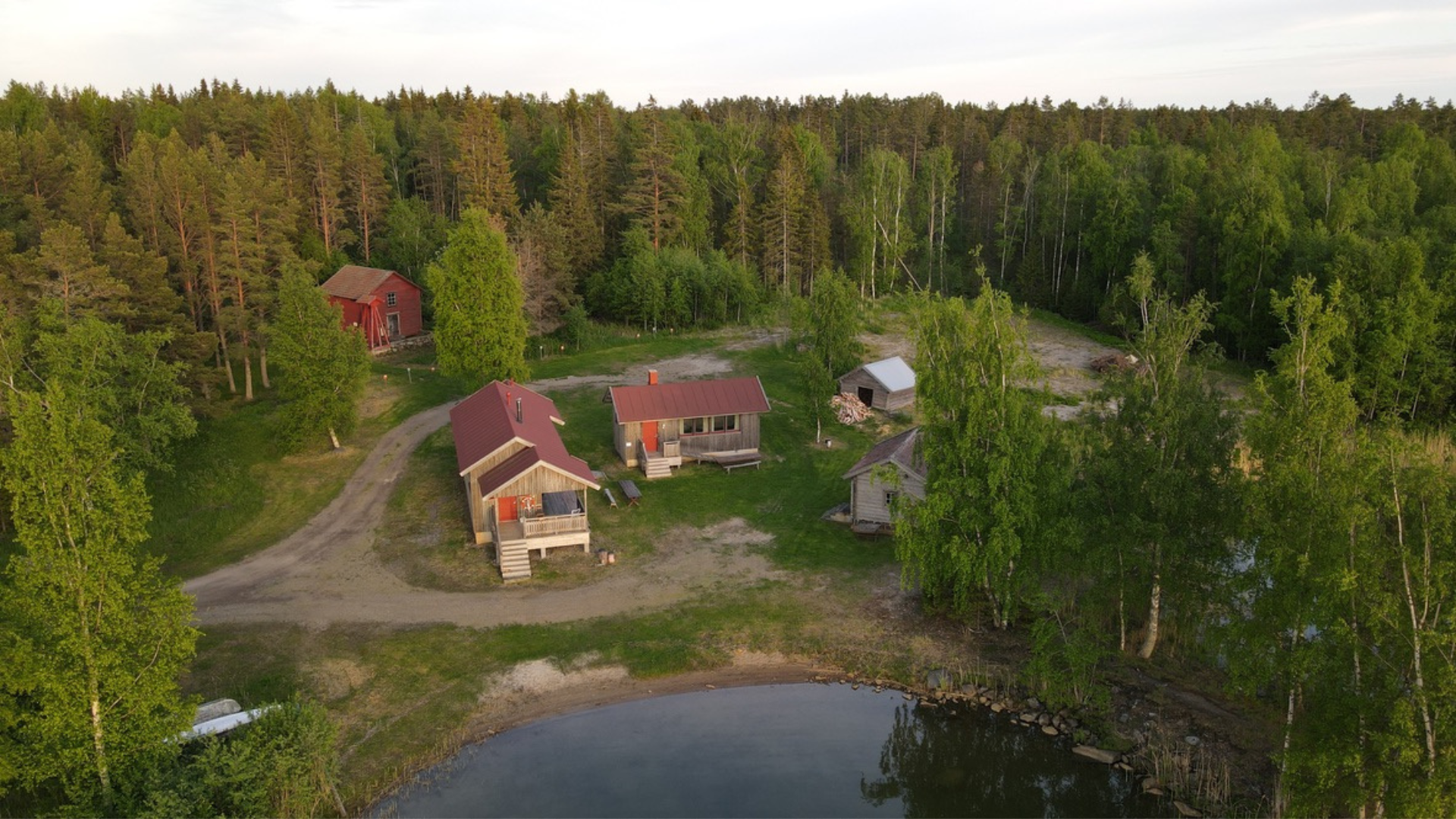 Flygbild över Kilens bastuområde med bastuhus, gillestuga och närliggande skog vid strandkanten.