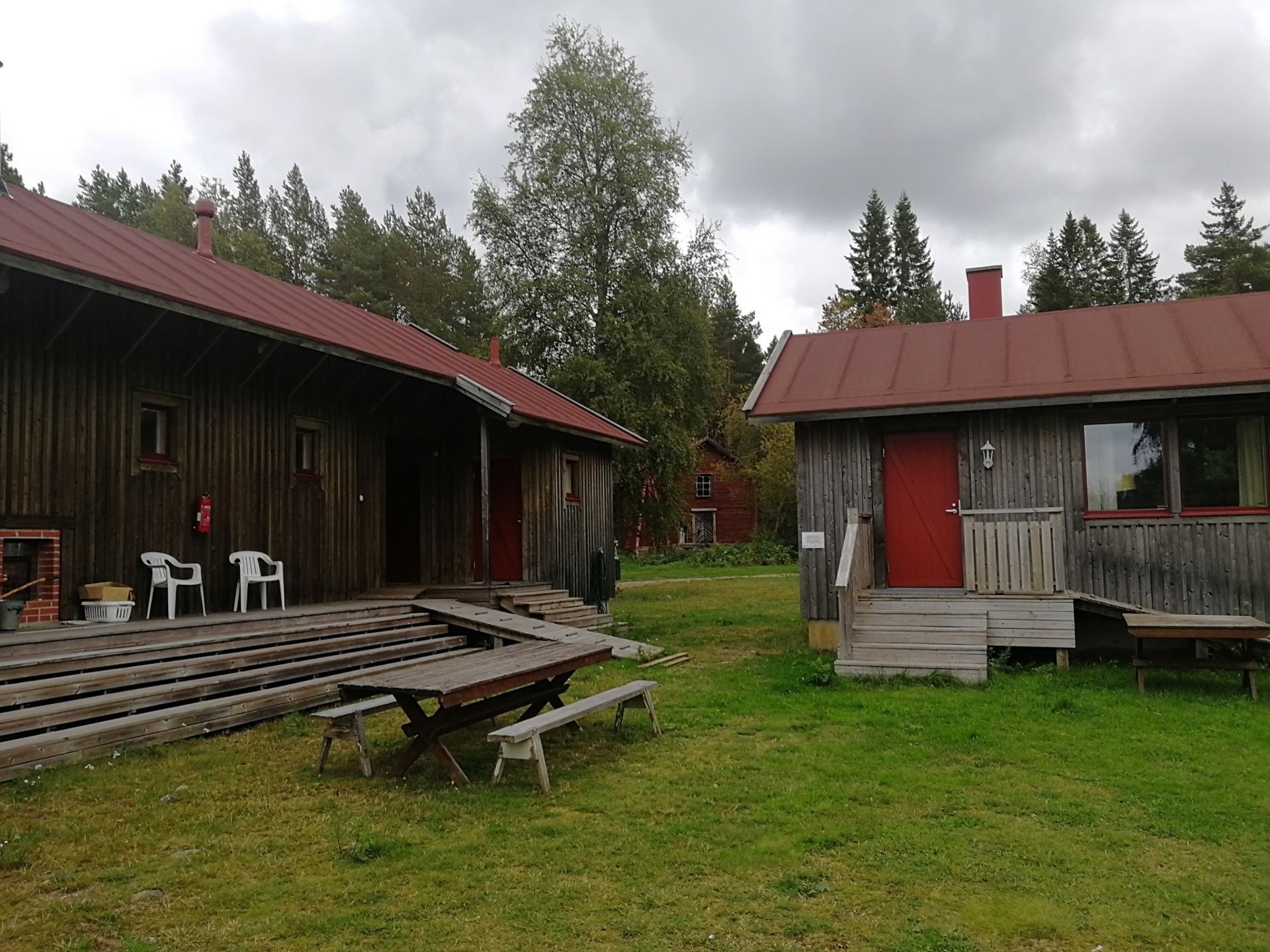 Bastuområde med två träbyggnader med röda plåttak och grön gårdsplan.
