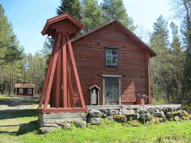 Rött träkapell med fristående klocktorn, beläget i skogsmiljö