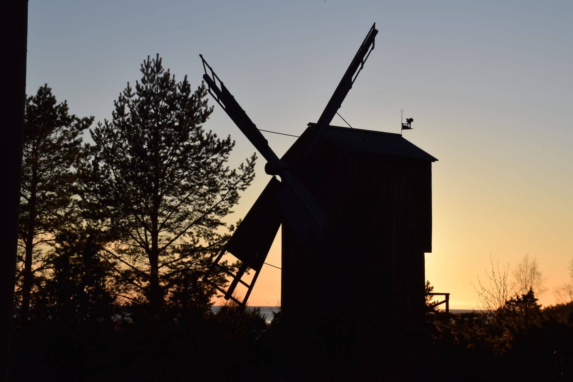 Siluett av en väderkvarn i solnedgång med träd i bakgrunden.